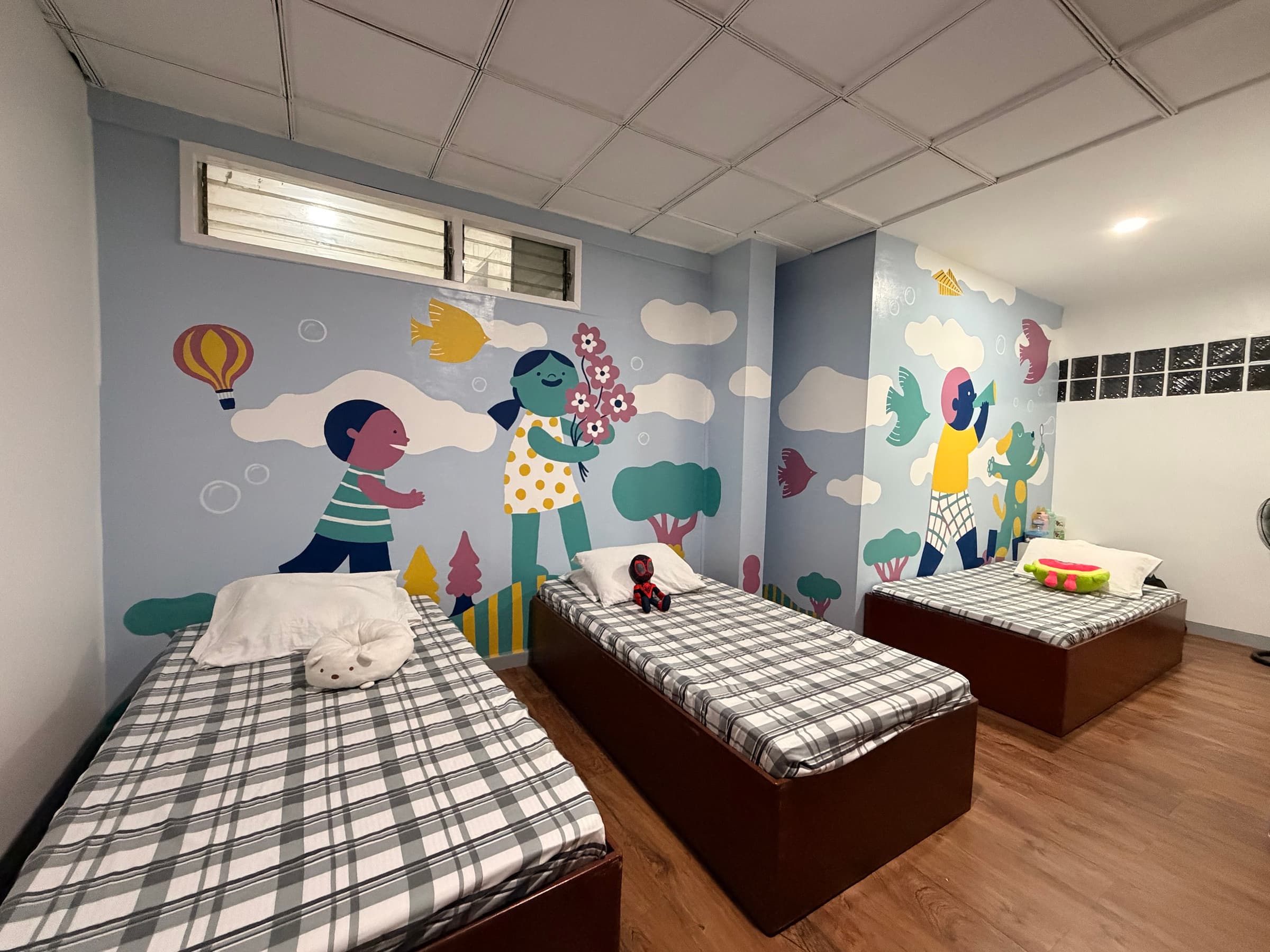 A bedroom with three beds and a colorful wall mural inside the Little Ark home